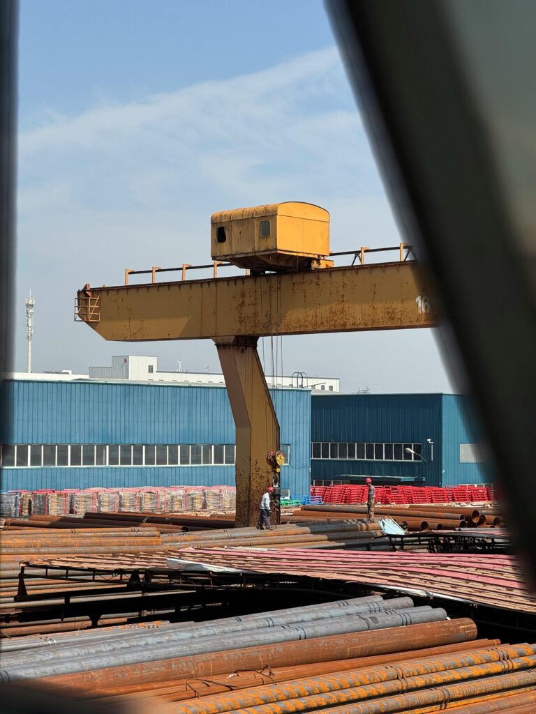A large industrial crane at a steel factory yard with workers, showcasing heavy machinery operations.