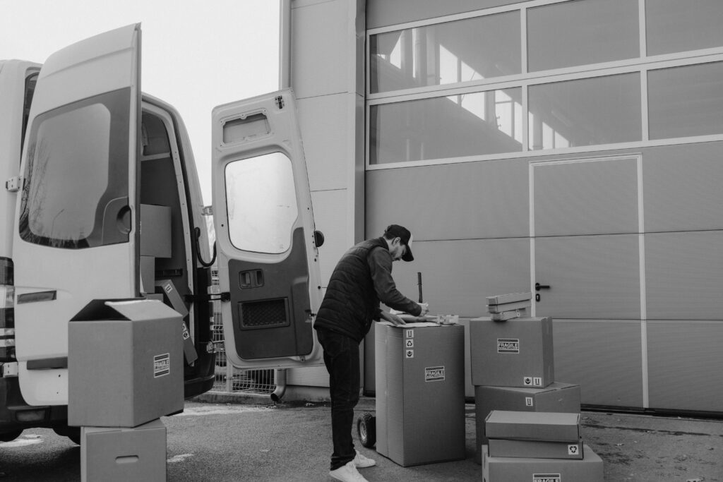 pexels photo 6169058 6169058 Monochrome image of a courier managing packages outside a warehouse, illustrating logistics workflow.
