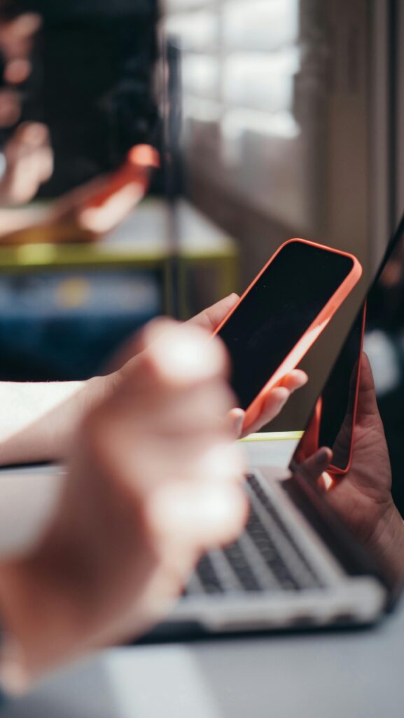 pexels photo 7054532 7054532 Hands holding smartphone near laptop, showcasing multitasking and technology use.